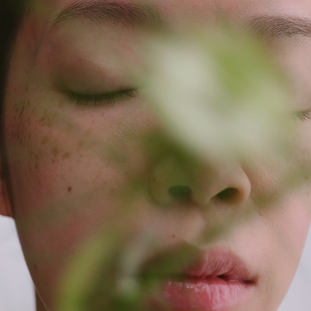 Close-up of a person's face with closed eyes and a green leaf in front.