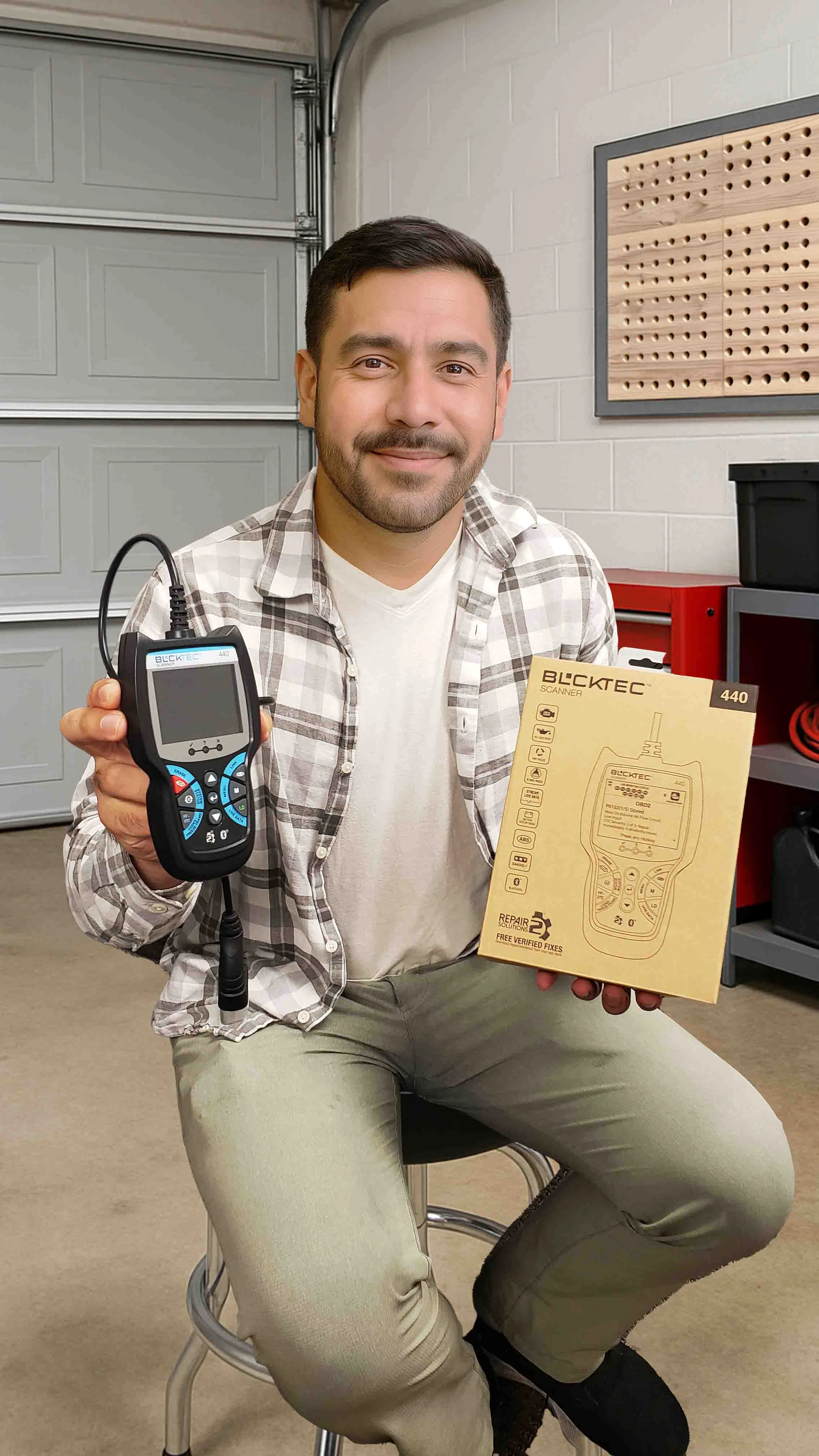 Person holding a diagnostic scanner and its packaging in a garage.