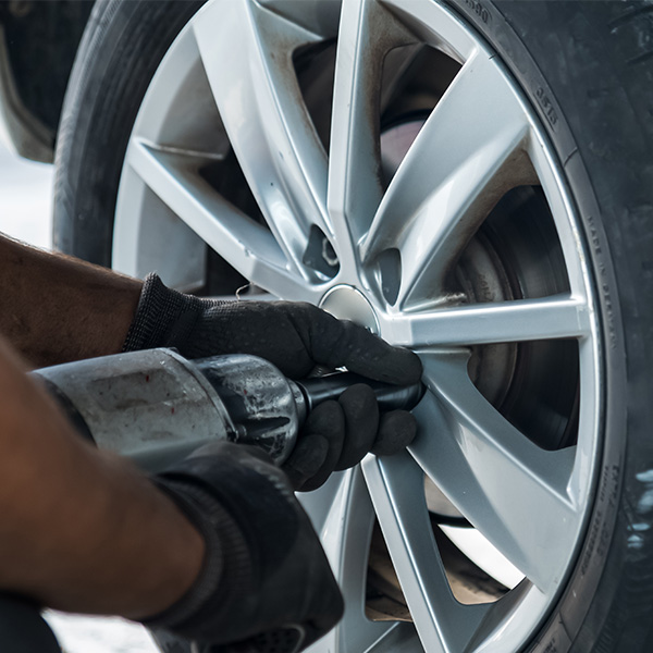 Mechanic using a power tool to tighten a car wheel lug nut.
