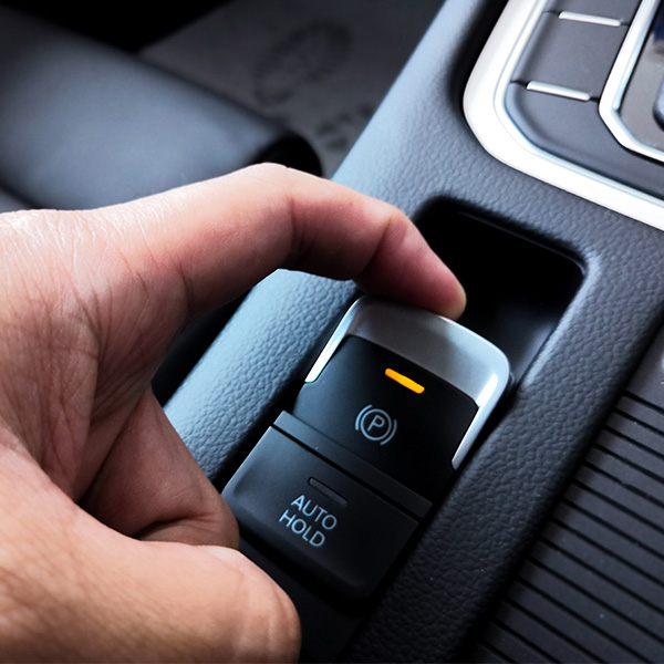 Hand operating a car's electronic parking brake button.