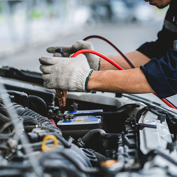 Person jump-starting a car battery with jumper cables.
