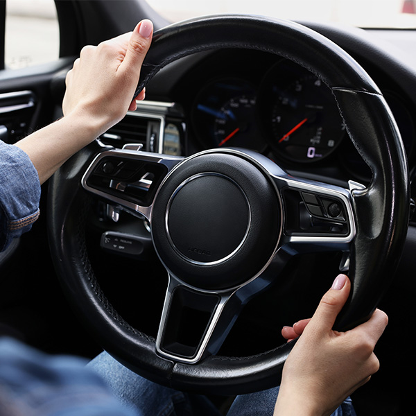 Hands holding a car steering wheel, dashboard visible.