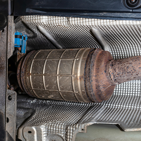 Close-up of a car's catalytic converter with a metal casing and rusted pipe.