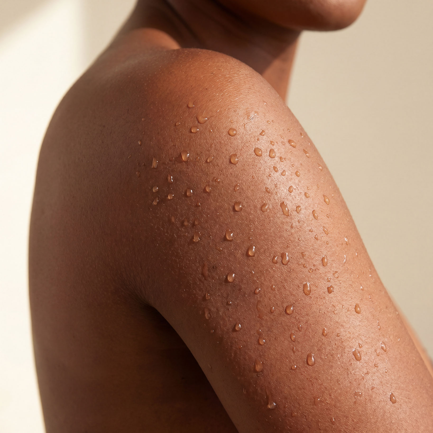 A close-up of water droplets beading on the skin of a person's shoulder and upper arm.