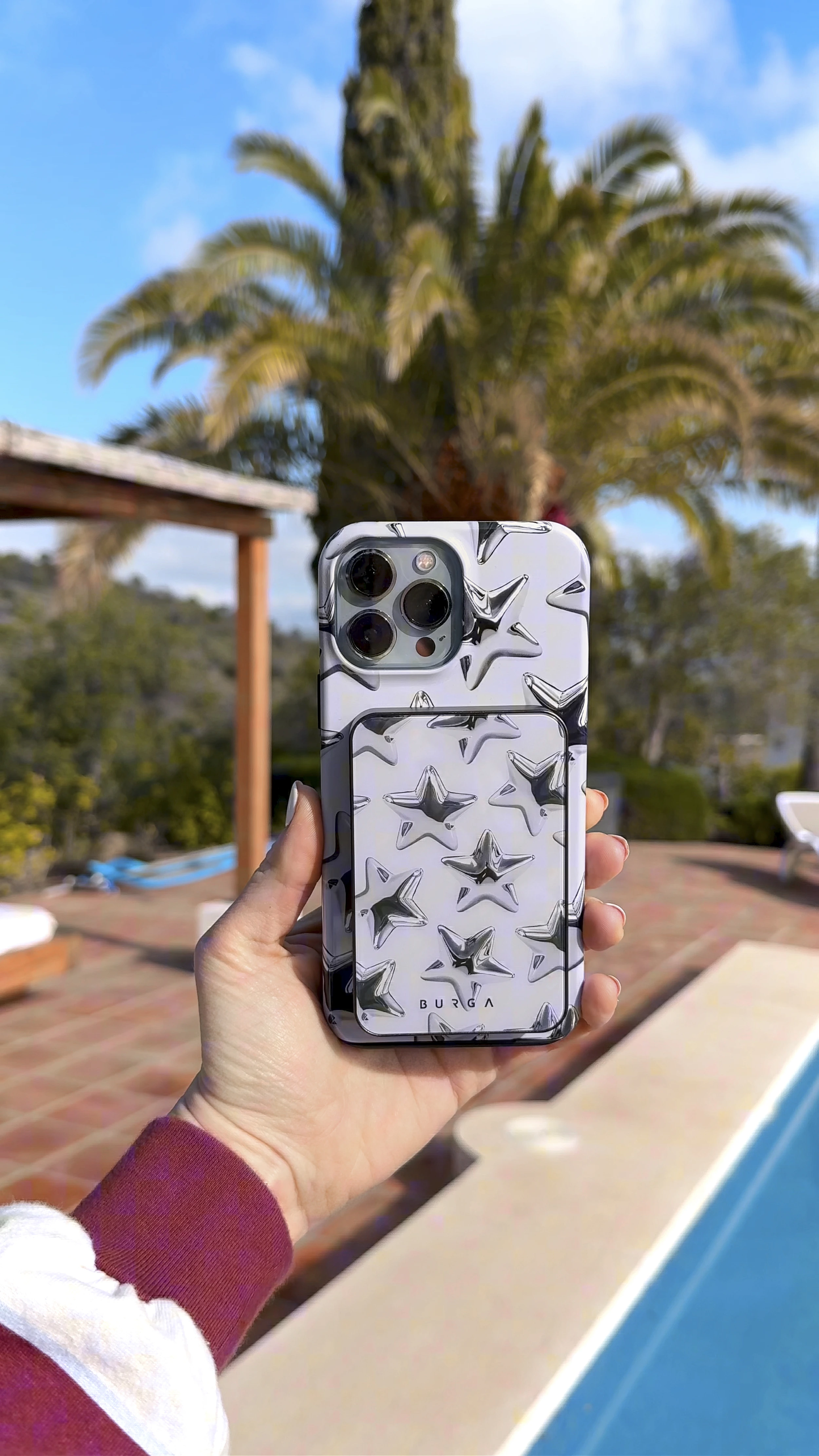Hand holding a phone with a star-patterned case by a poolside.