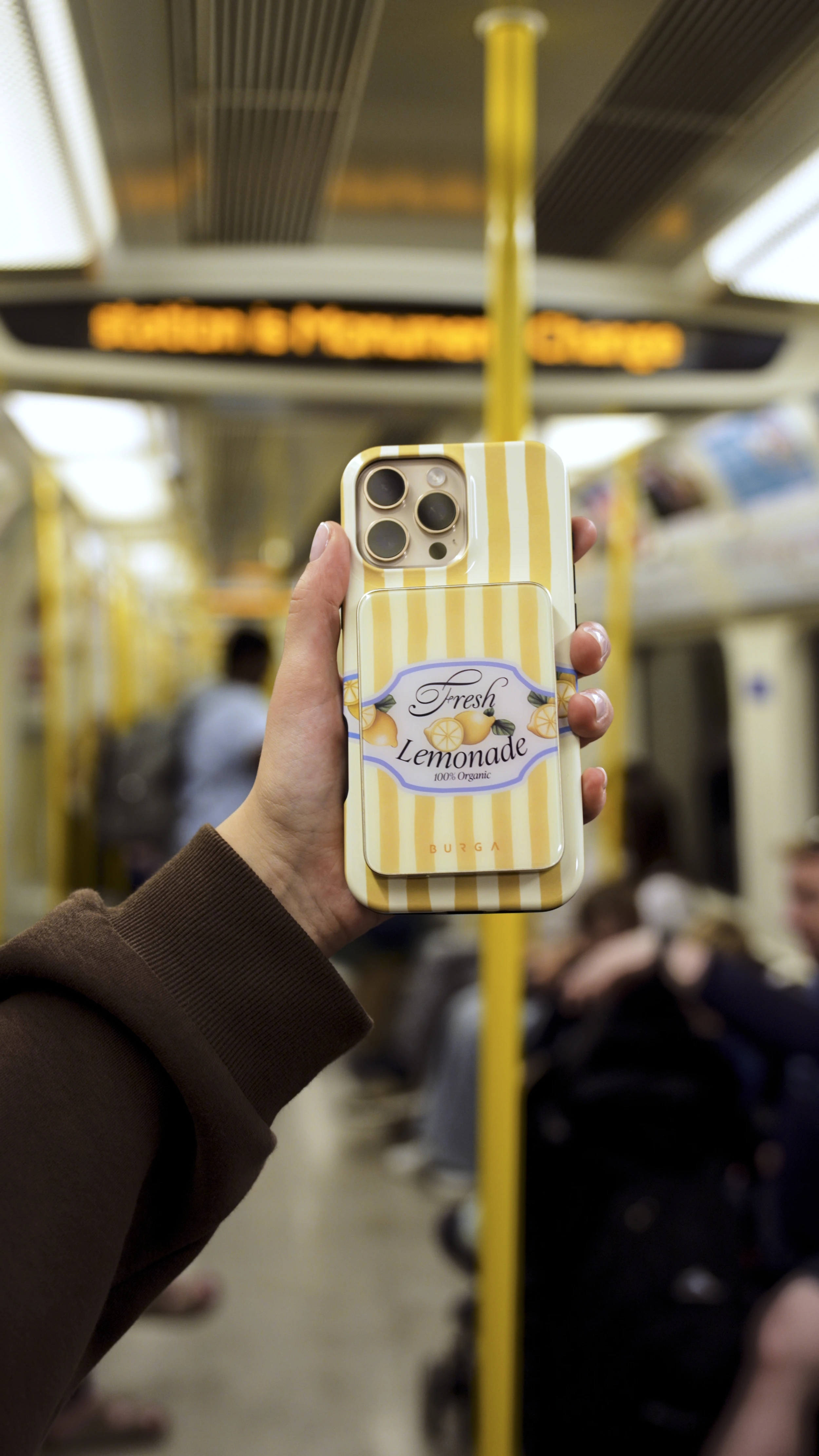 Hand holding a phone with a lemonade-themed case on a train.