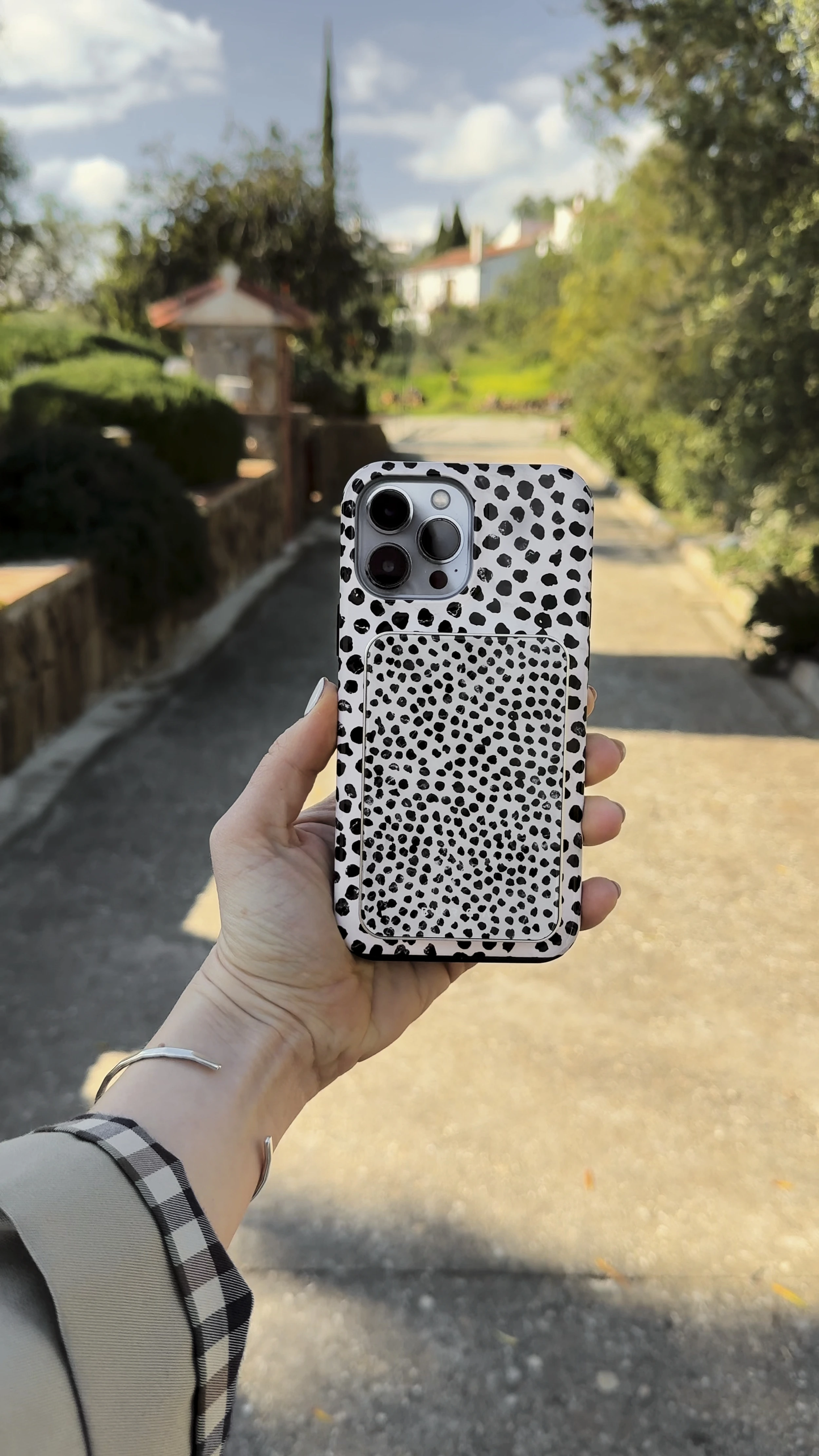 Hand holding a phone with a black and white spotted case outdoors.