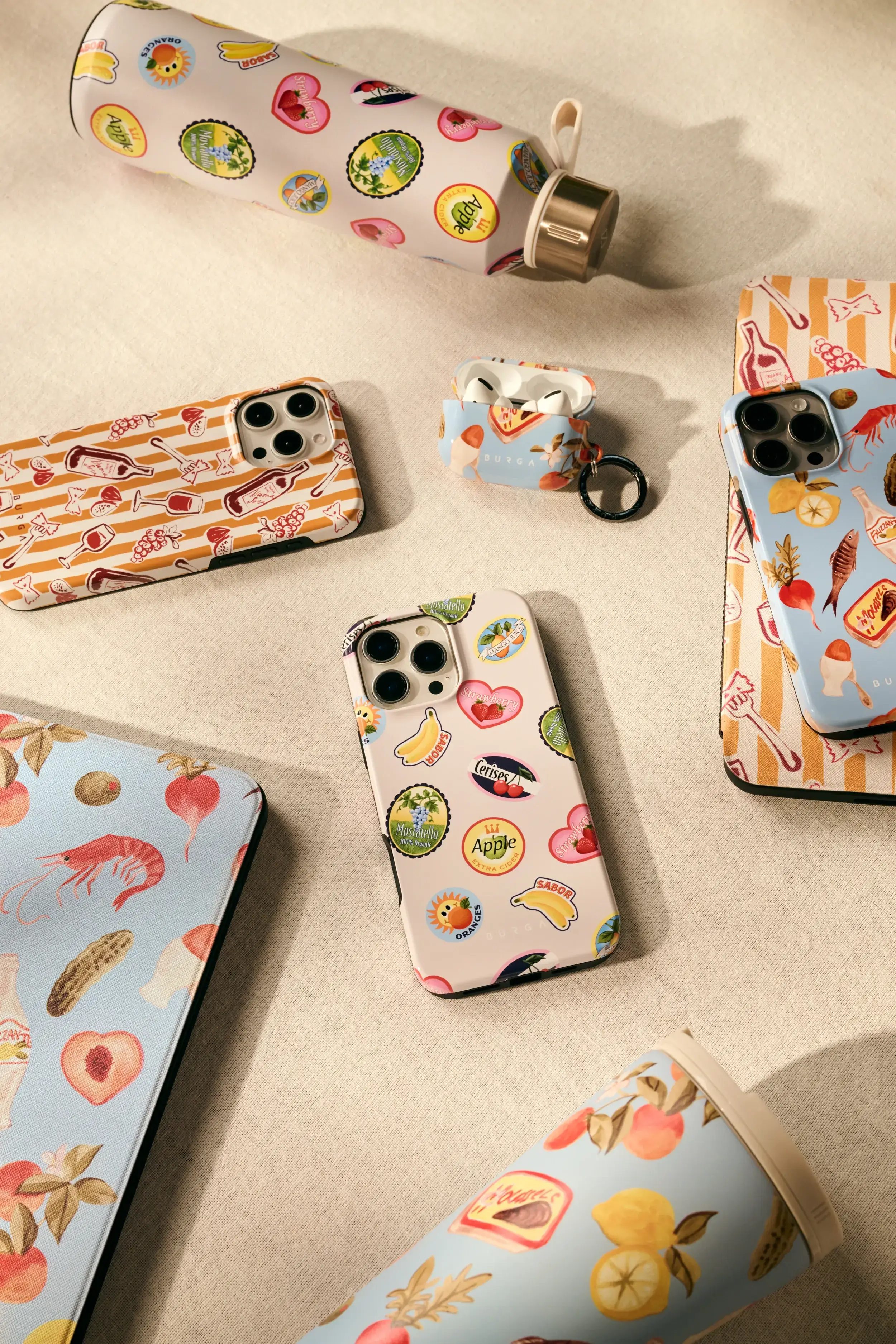 Colorful phone cases, water bottles, and AirPods case with fruit and food designs on a beige background.