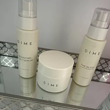 Three DIME skincare products on a mirrored surface.