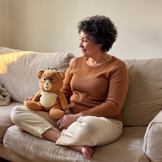 Woman sitting on a couch with a teddy bear wearing glasses.