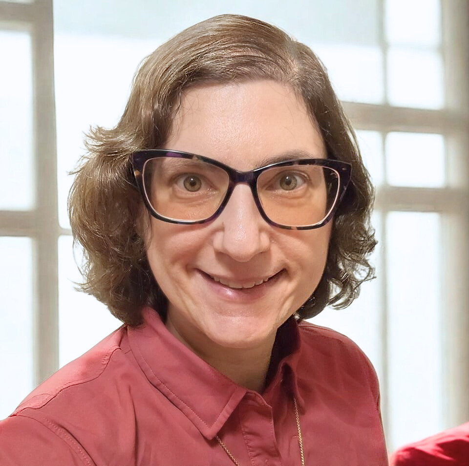 Person with glasses and short hair smiling indoors.