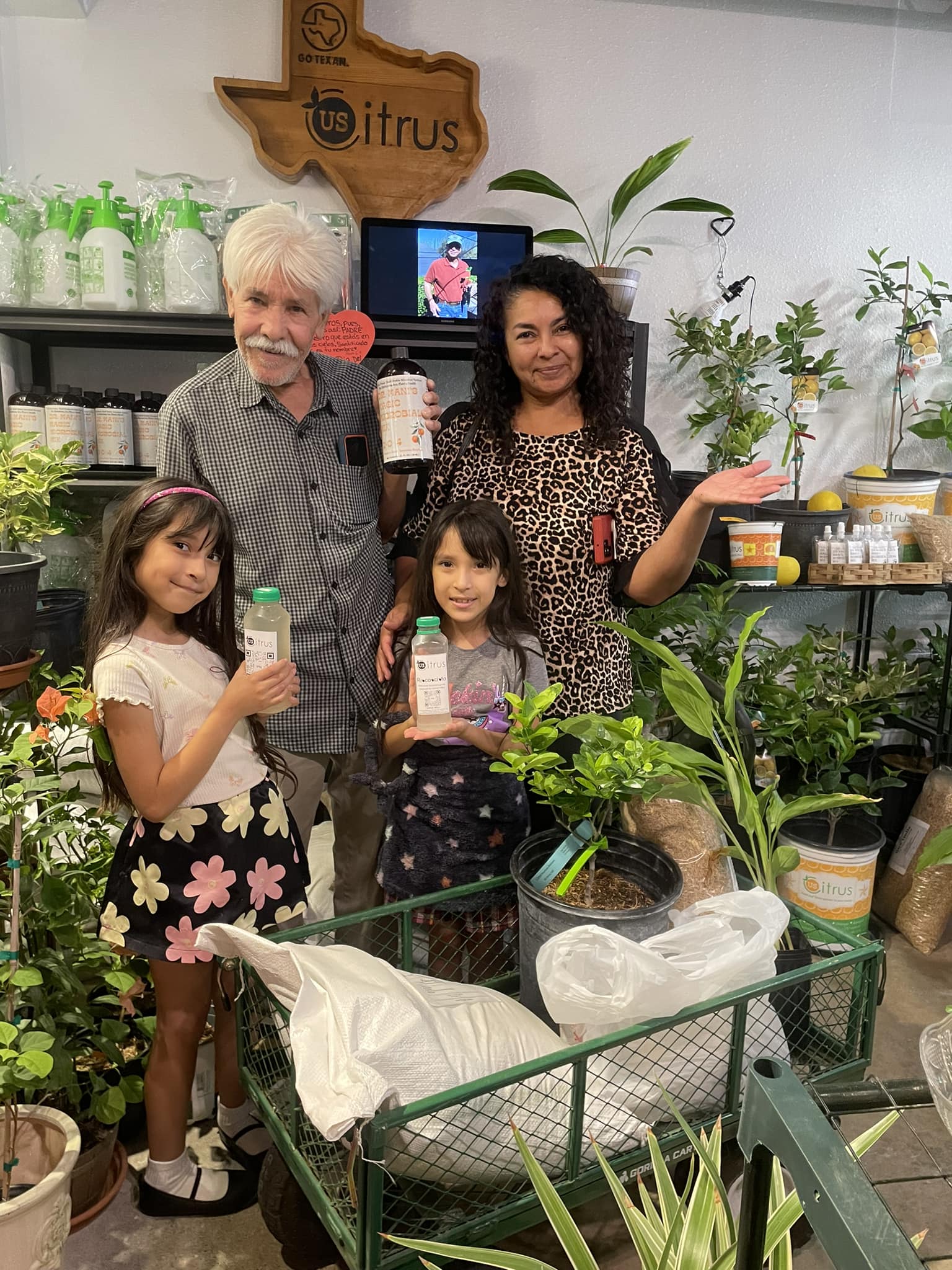 A family of four poses for a photo inside a plant store, holding various bottled products.