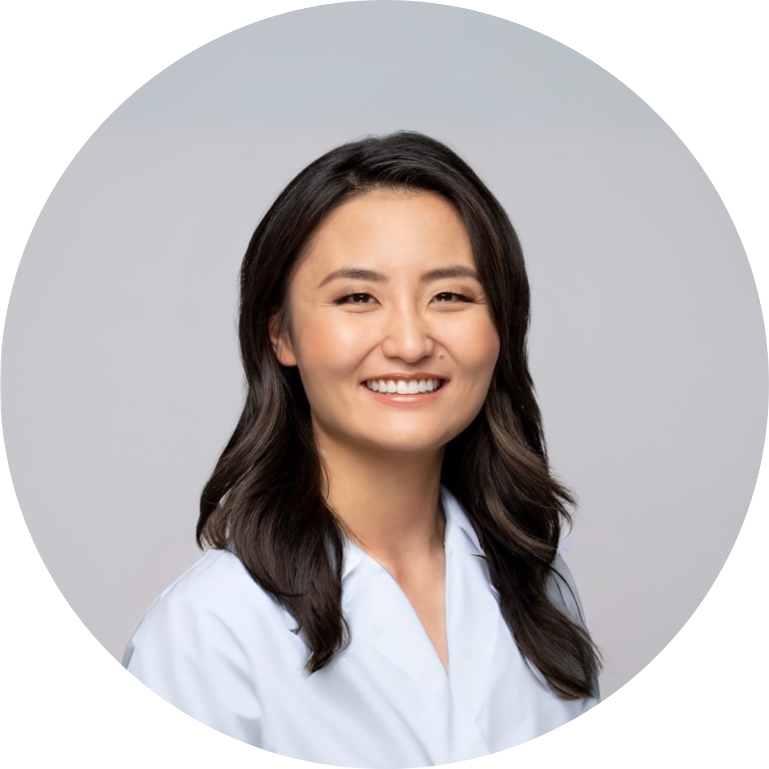 Smiling person with long hair wearing a white coat against a plain background.