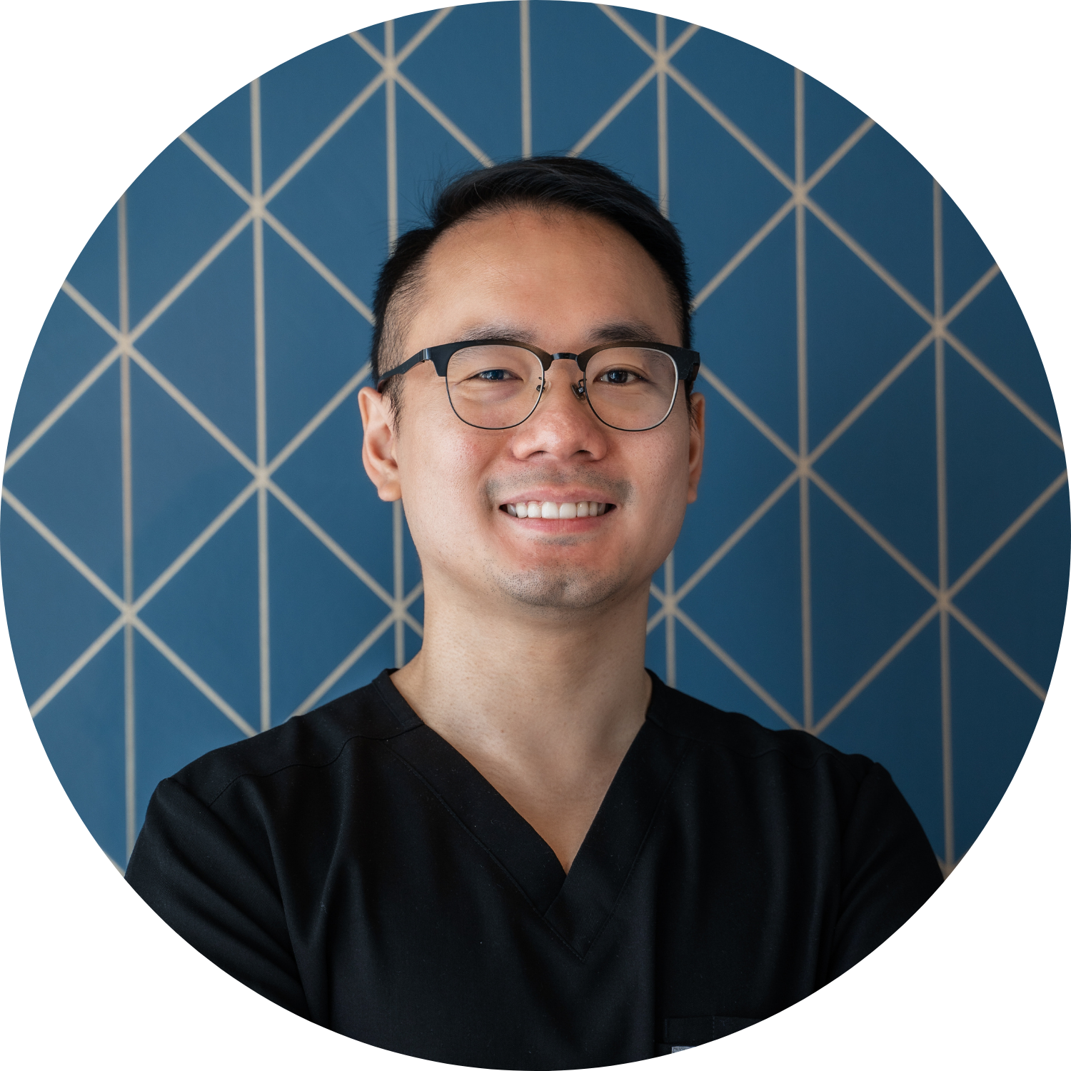 Person with glasses smiling in front of a blue geometric wall.