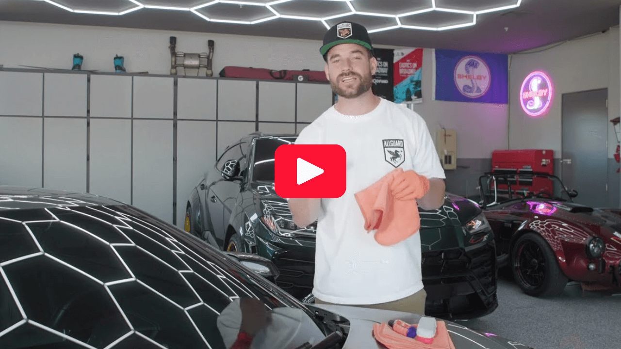 Man in a garage holding a cloth, with cars and hexagonal lights.