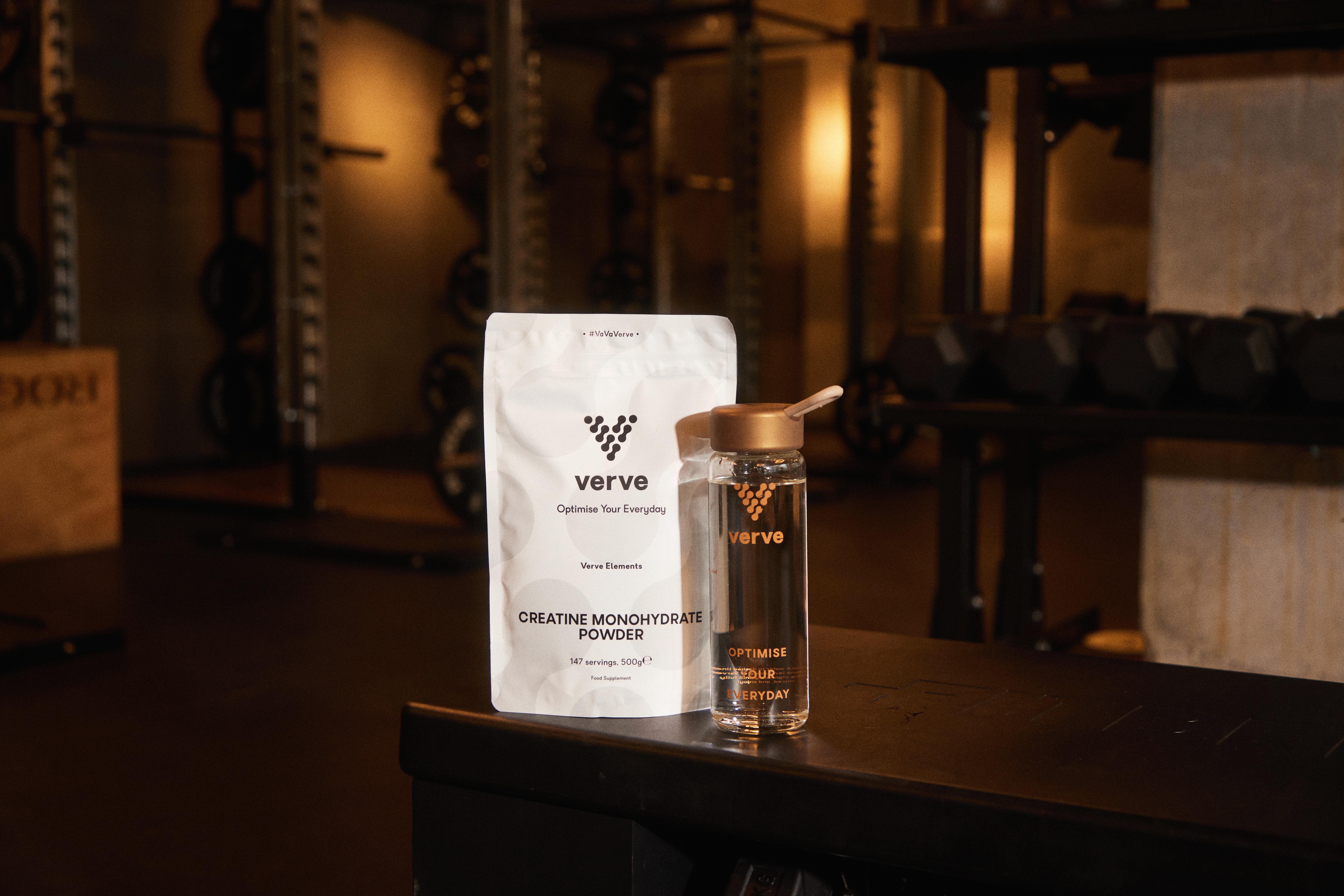 Creatine powder and water bottle on a gym counter with weights in the background.