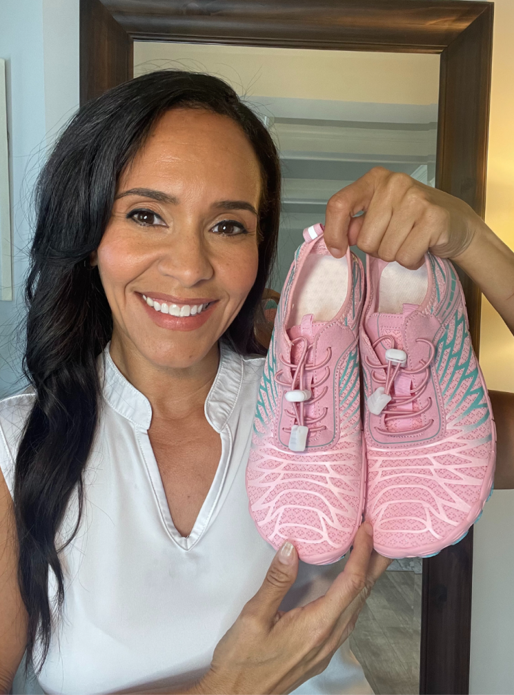 Person holding pink athletic shoes, smiling at the camera.