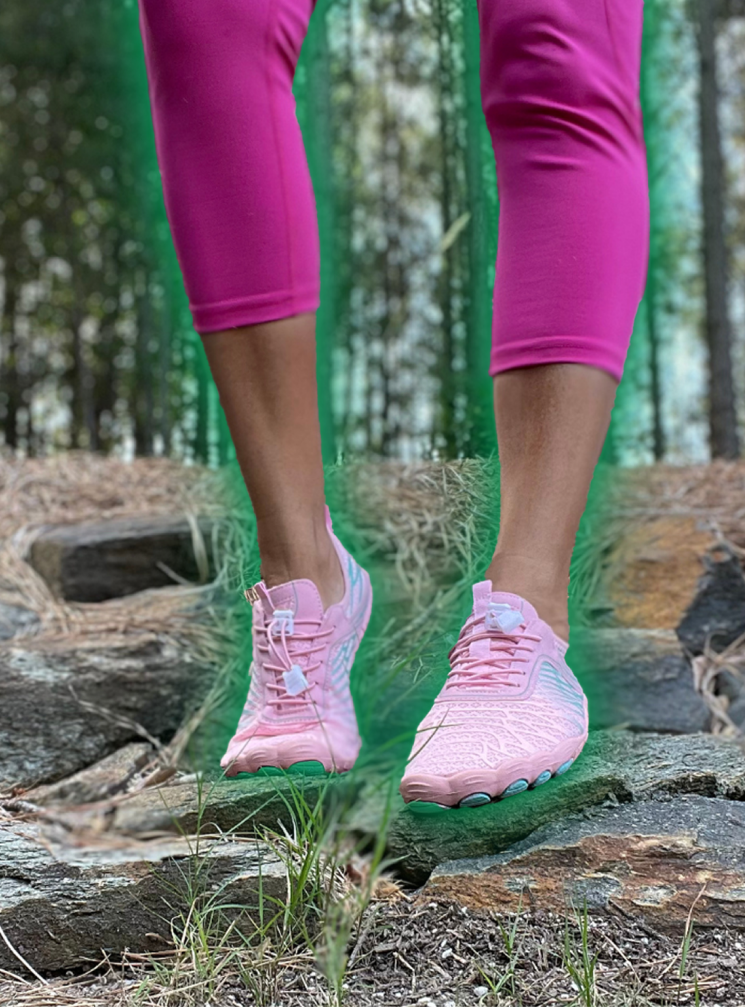 Person wearing pink leggings and shoes standing on rocks in a forest.