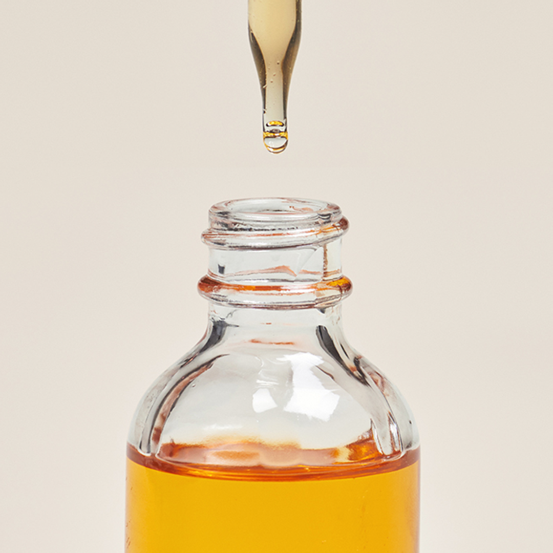 A dropper releasing liquid into a small bottle with orange liquid.