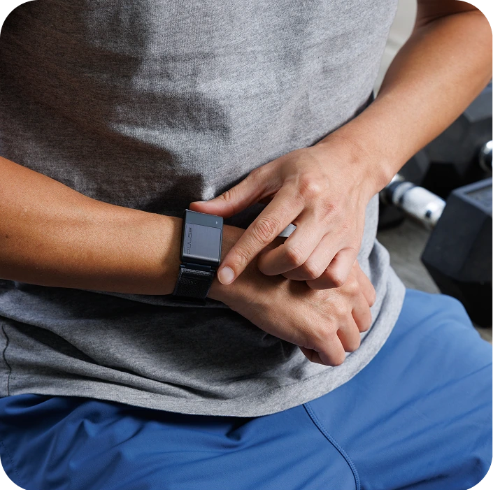 Person checking smartwatch, sitting with blue shorts, near gym equipment.