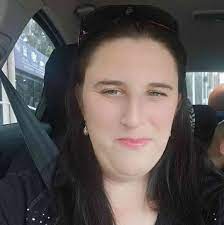 Person with long dark hair sitting in a car, wearing a black shirt.