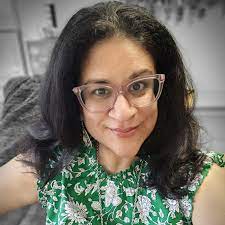 Person wearing glasses and a green floral top smiling at the camera.