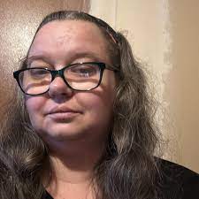 Person with glasses and long hair against a plain background.