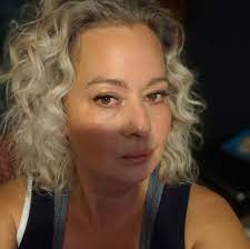 Person with curly, light hair and a dark shirt looking at the camera.