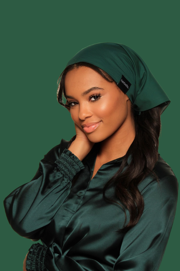 Woman in green headscarf and blouse, smiling with hand on cheek.