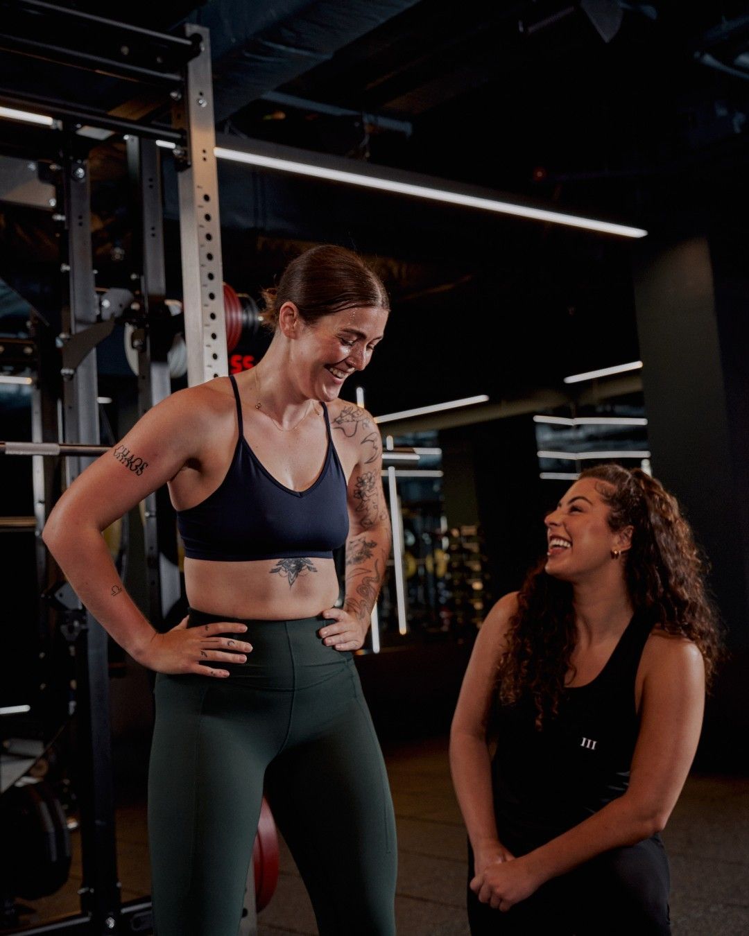 Two women smiling and talking in a gym setting.