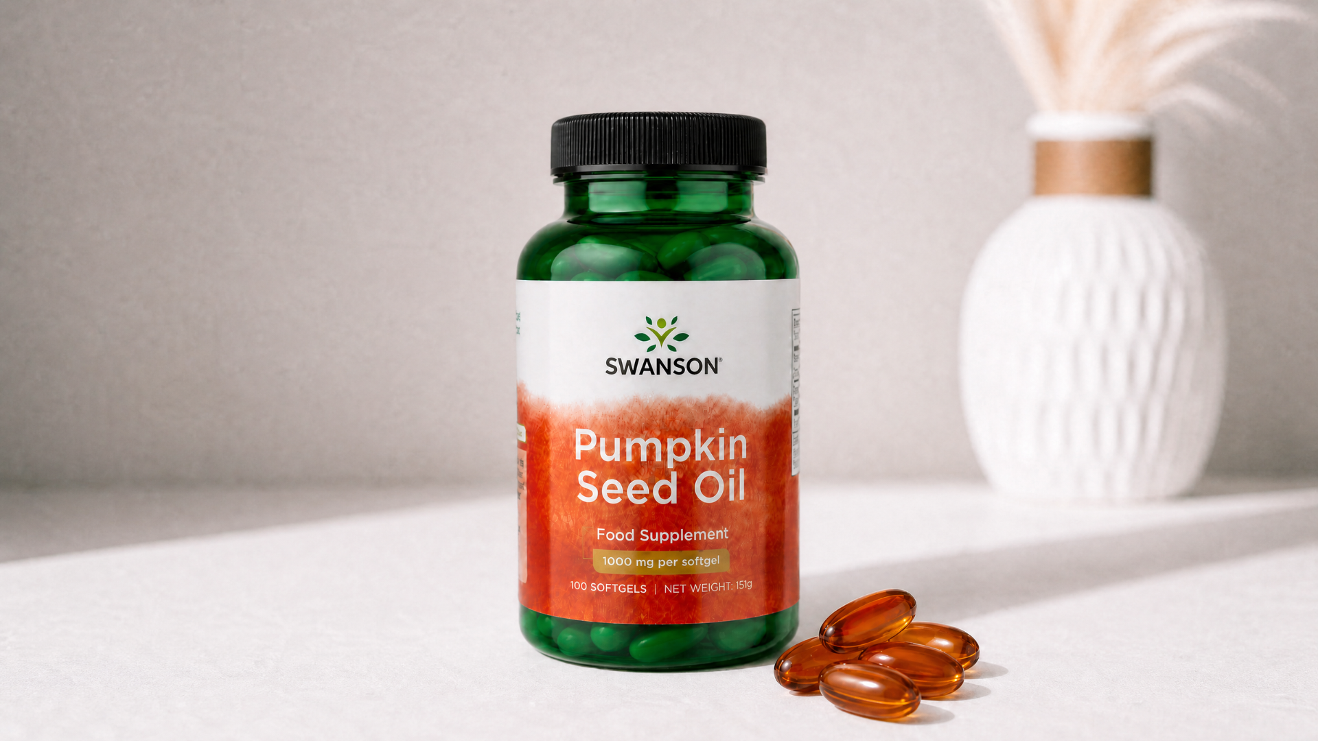 A green bottle of Swanson Pumpkin Seed Oil with several orange softgels spilled out on a table.