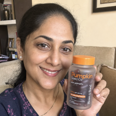 A smiling woman in a blue top holds up a bottle of Pumpkin Seed Oil supplements.