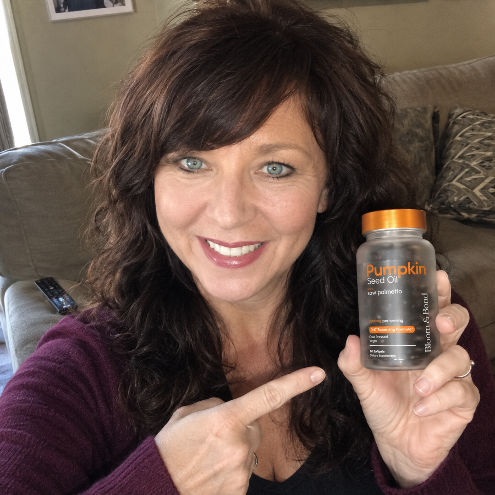 A smiling woman with brown hair holds up and points to a bottle of Pumpkin Seed Oil supplements.