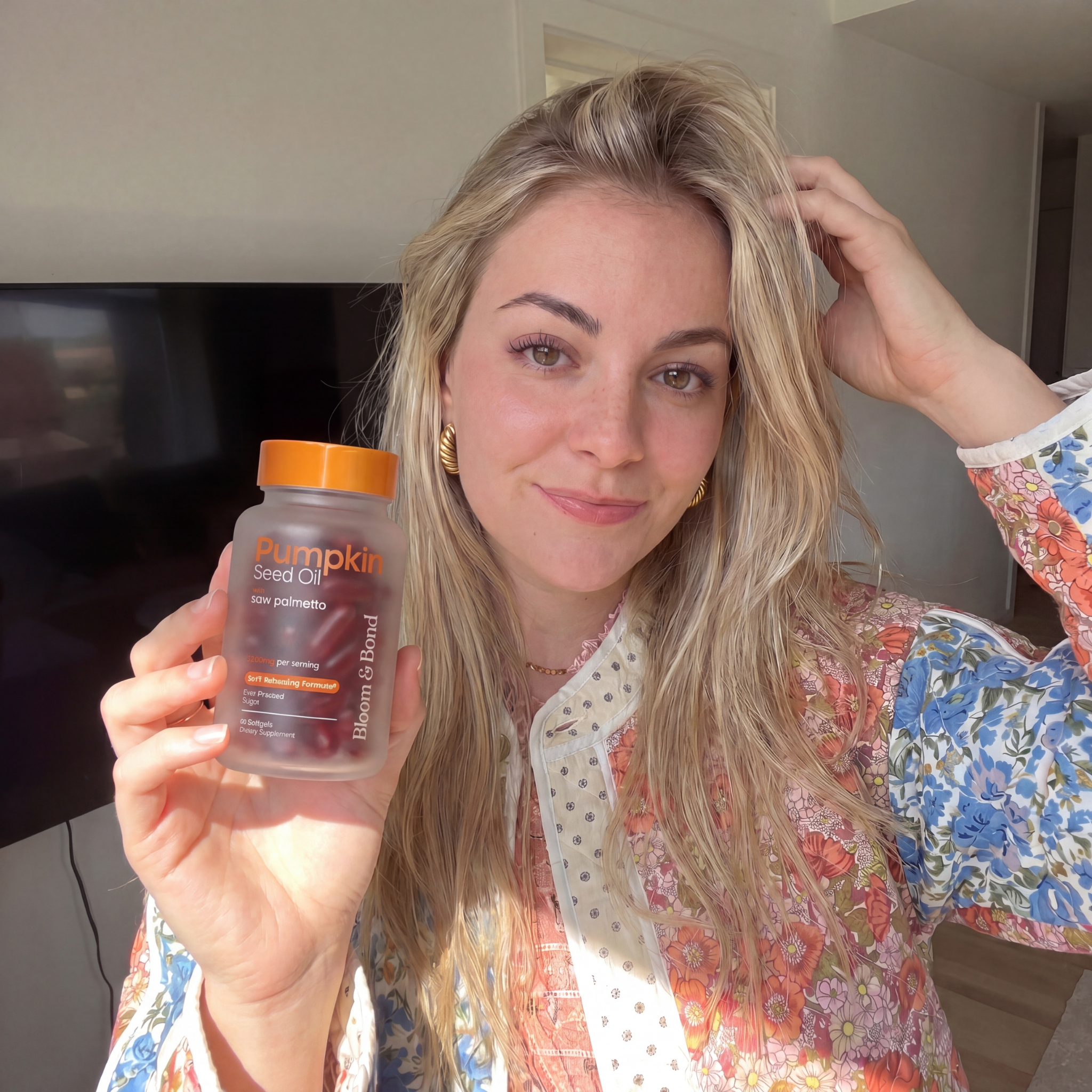 A blonde woman in a floral shirt holds up a bottle of Pumpkin Seed Oil supplements.