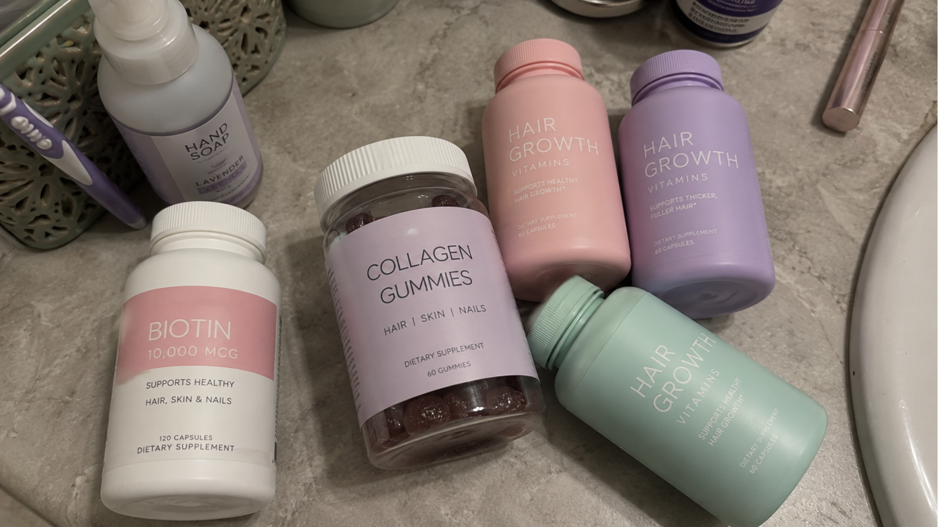 Several bottles of hair growth vitamins, biotin, and collagen gummies arranged on a bathroom counter.