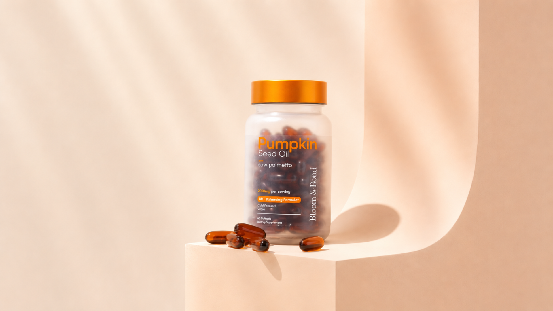 A bottle of Bloom & Bond Pumpkin Seed Oil softgels sits on a peach-colored stand with some capsules scattered.