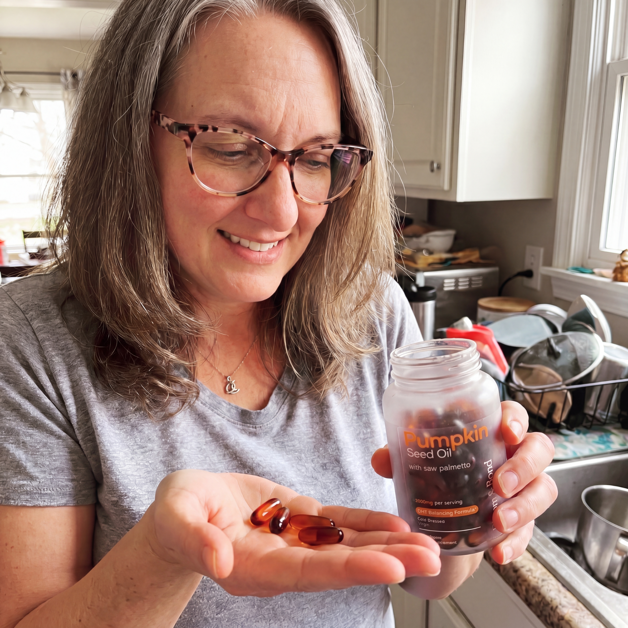 A smiling woman with glasses holds a bottle of Pumpkin Seed Oil, looking at the capsules in her palm.