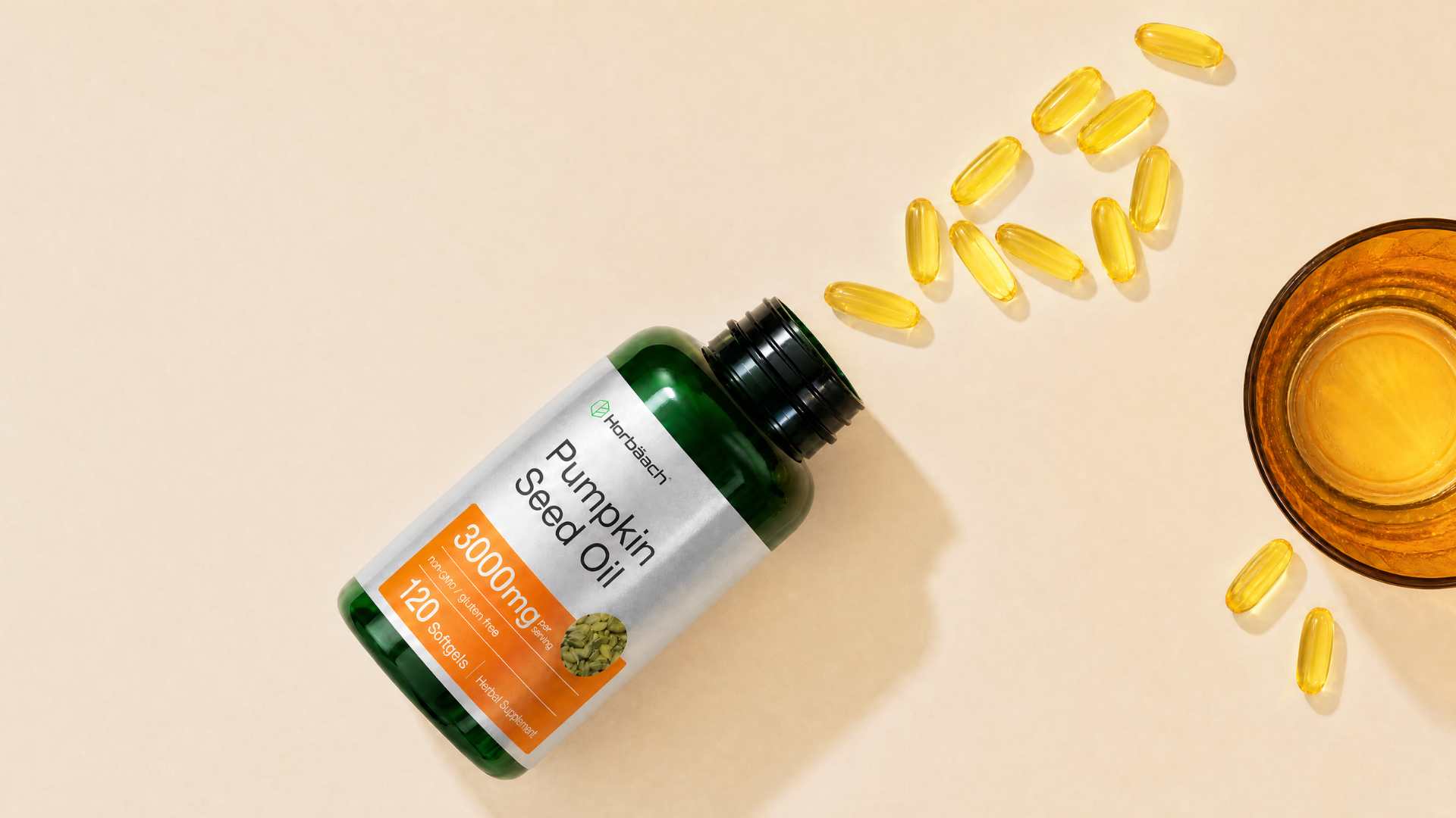 A bottle of Horbäach Pumpkin Seed Oil softgels spilled onto a surface next to a glass.