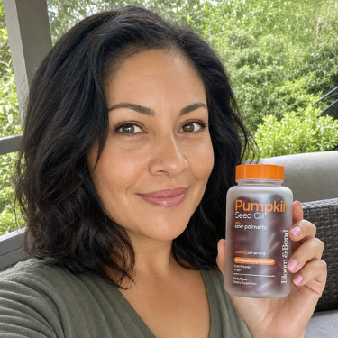 A smiling woman with dark hair holds up a bottle of Bloom & Bond Pumpkin Seed Oil.