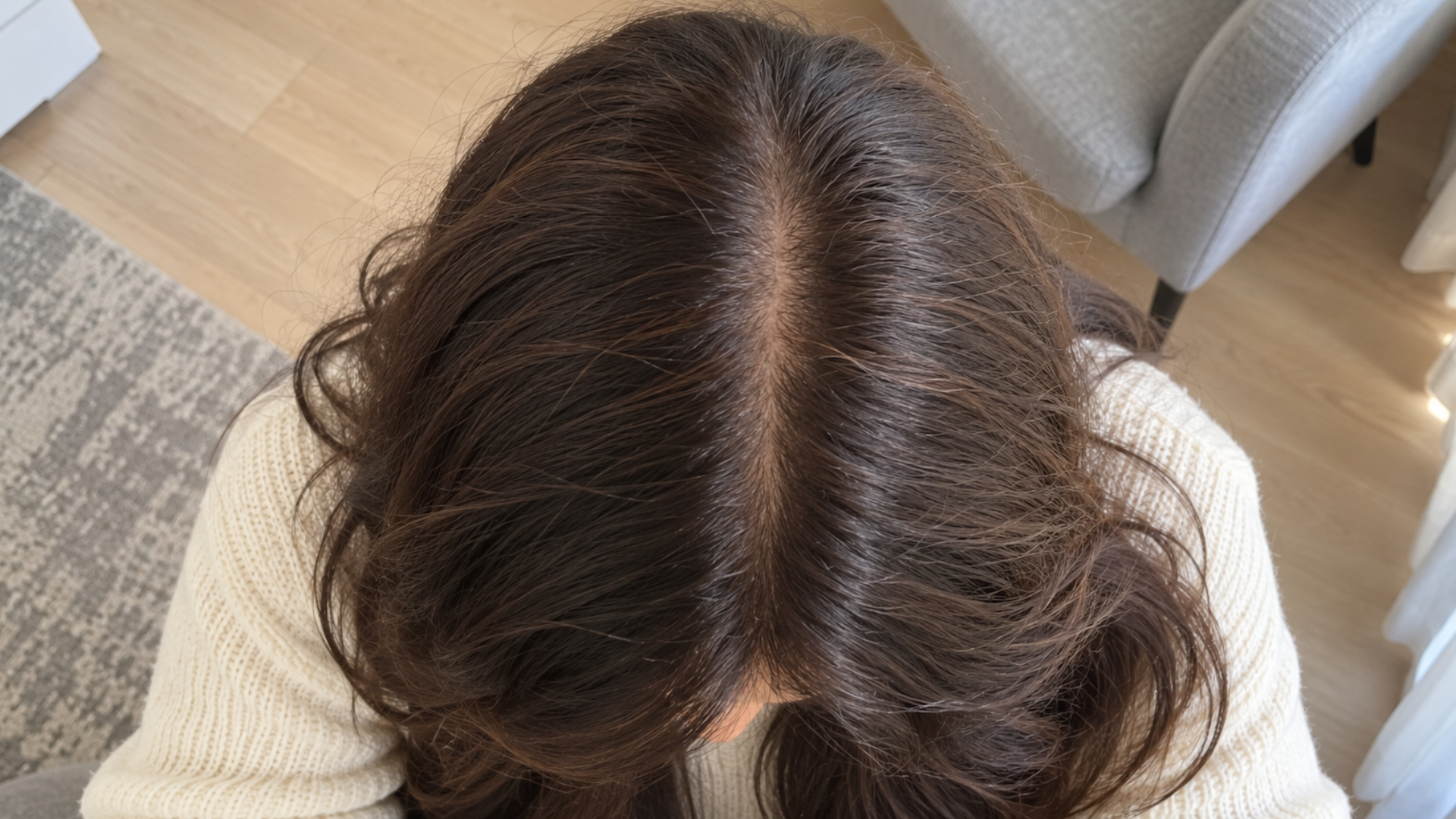 An overhead view of the top of a person's head with dark brown hair parted in the center.