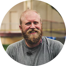 A bearded man smiling outdoors in casual attire.