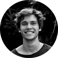 A person smiling outdoors in a black and white photograph.