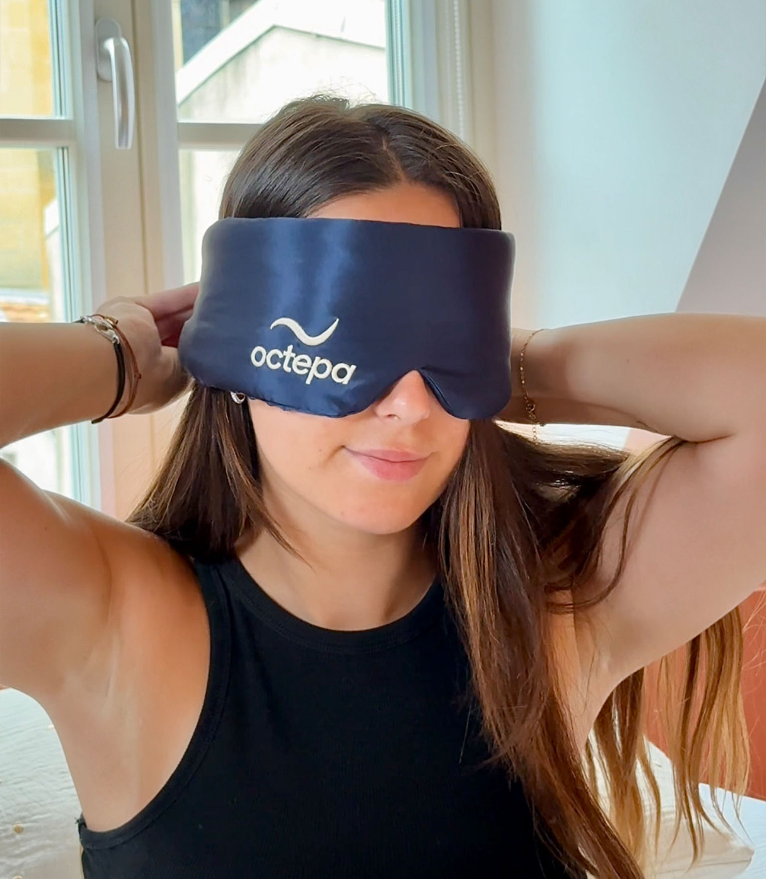 Person wearing a black sleep mask with 'octepa' logo, near a window.