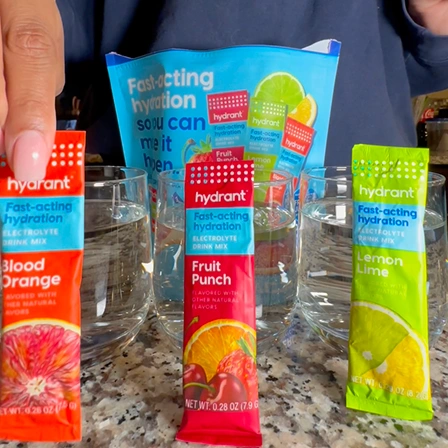 Packets of Hydrant electrolyte drink mix in various flavors are displayed in front of glasses of water.