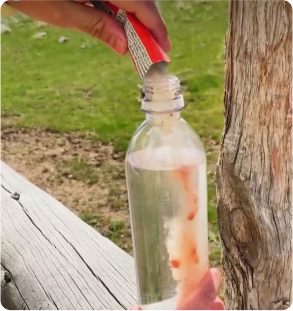 Person pouring powder into a water bottle outdoors.