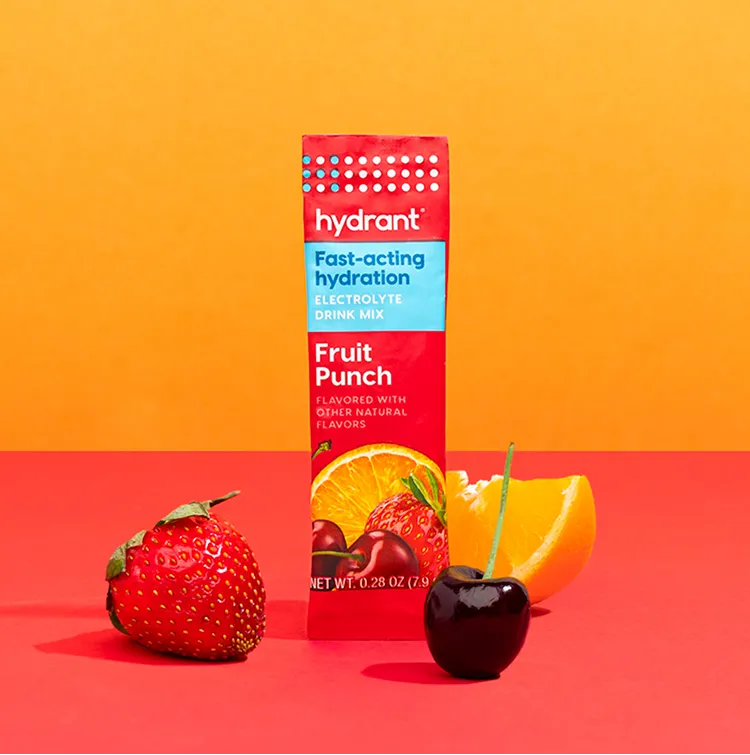 A packet of Hydrant Fruit Punch electrolyte mix next to a strawberry, cherry, and an orange wedge.