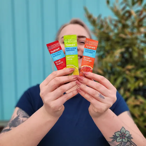 A person with tattoos holds up three packets of Hydrant drink mix in different flavors.