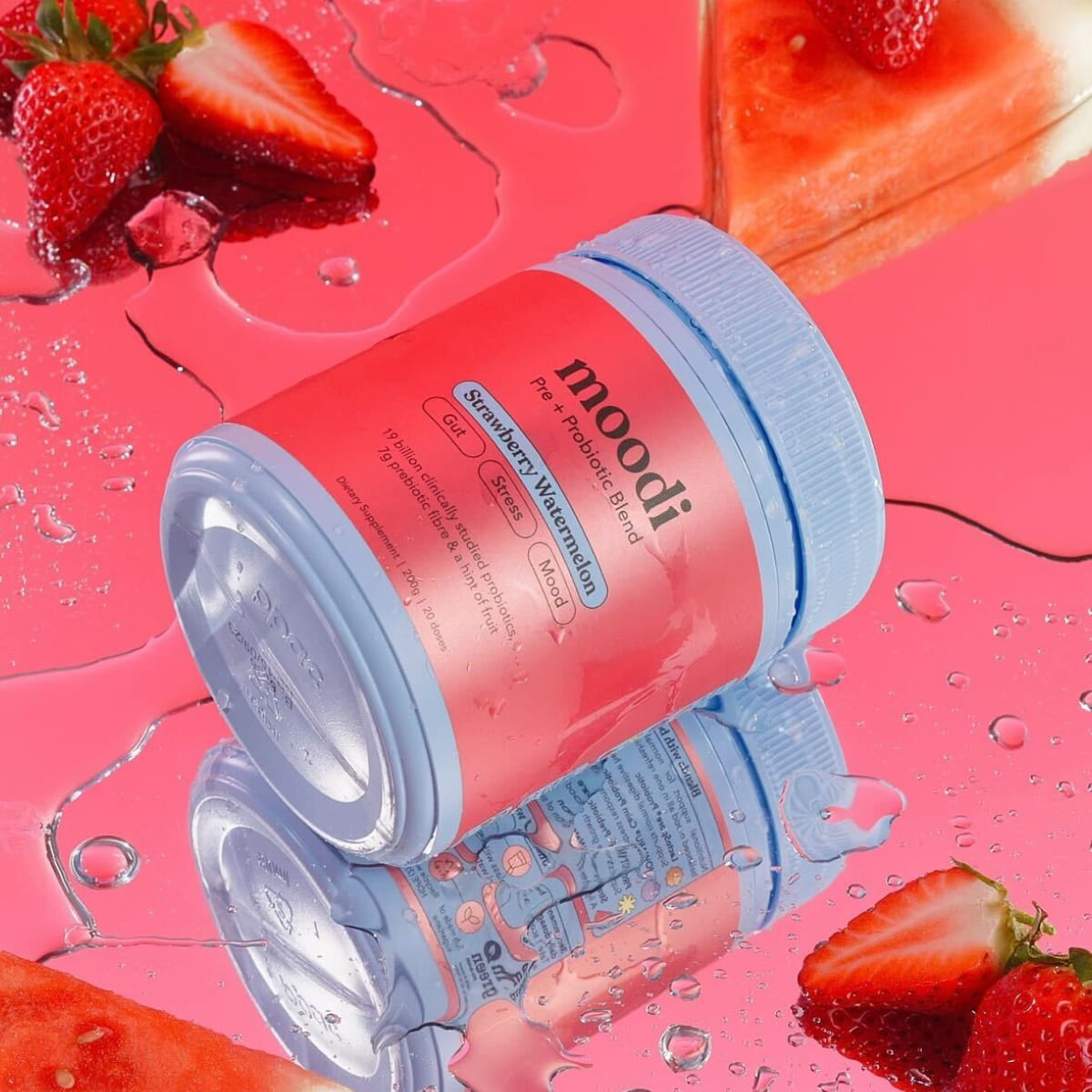Jar of 'moodi' probiotic blend with strawberries and watermelon slices on pink surface.