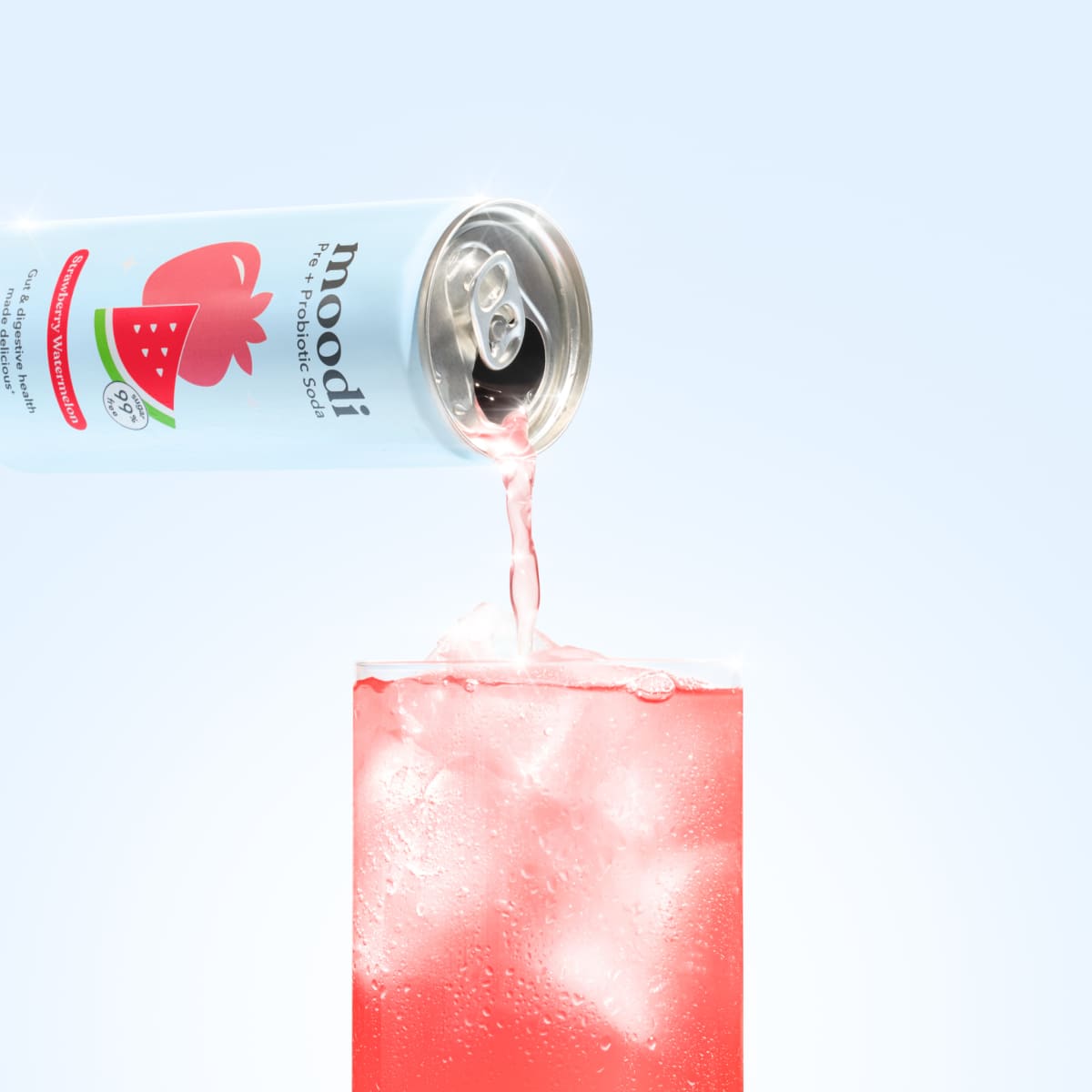 A can pouring pink liquid into a glass filled with ice cubes.
