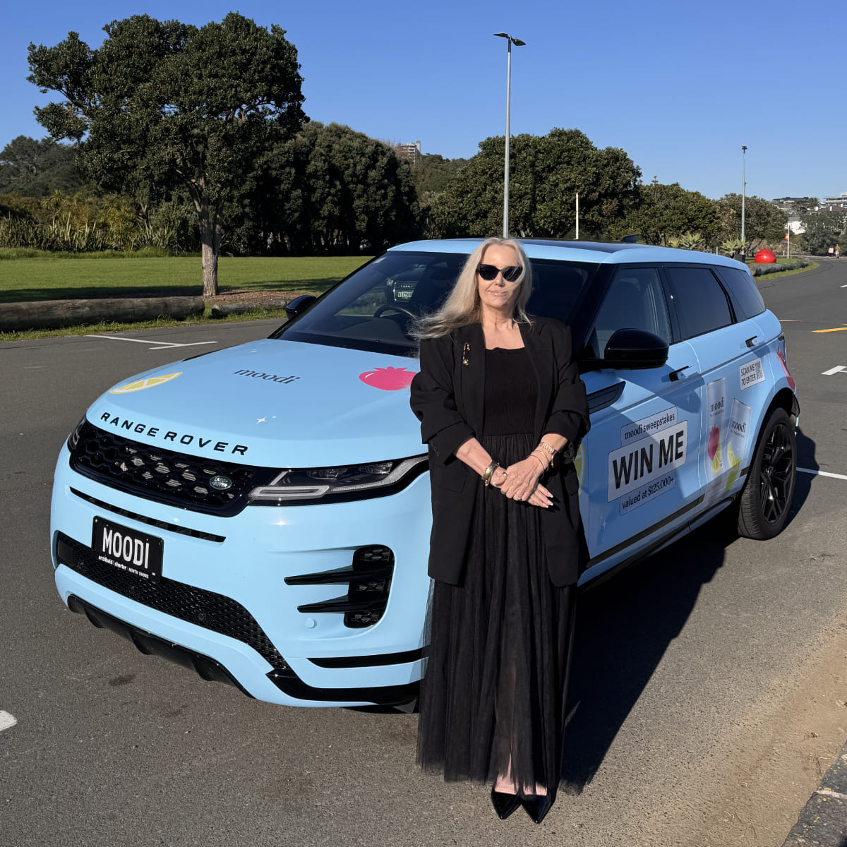 Person in black dress standing beside a blue Range Rover with promotional decals.